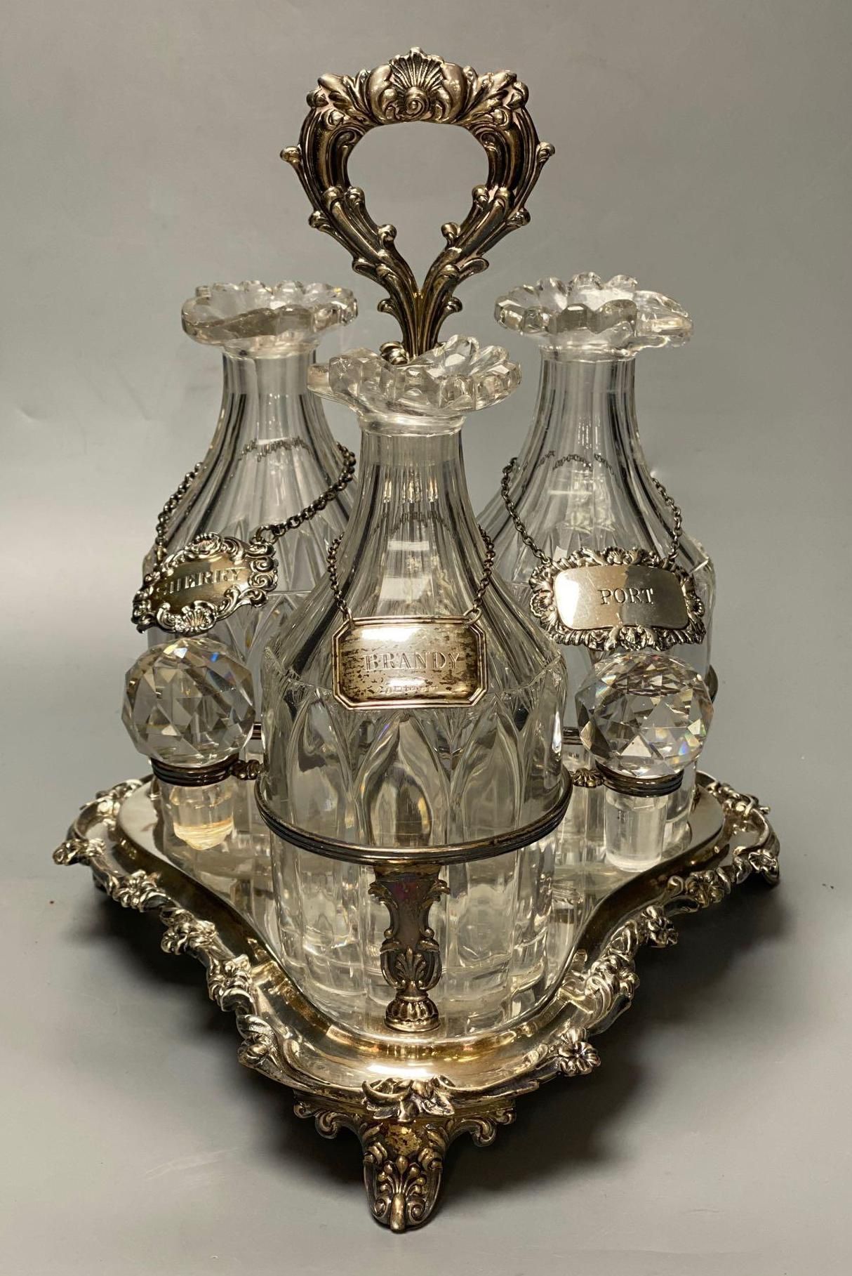 A set of three early 19th century glass decanters, now with facetted stoppers, and a silver label, on later silver plated decanter stan